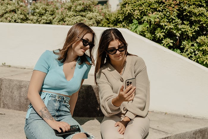 to unge damer ser på mobilen i solen ute to unge damer ser på mobilen i solen ute